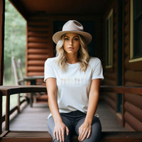 Woman wearing a white t-shirt with text and a beige hat sitting on a wooden porch.